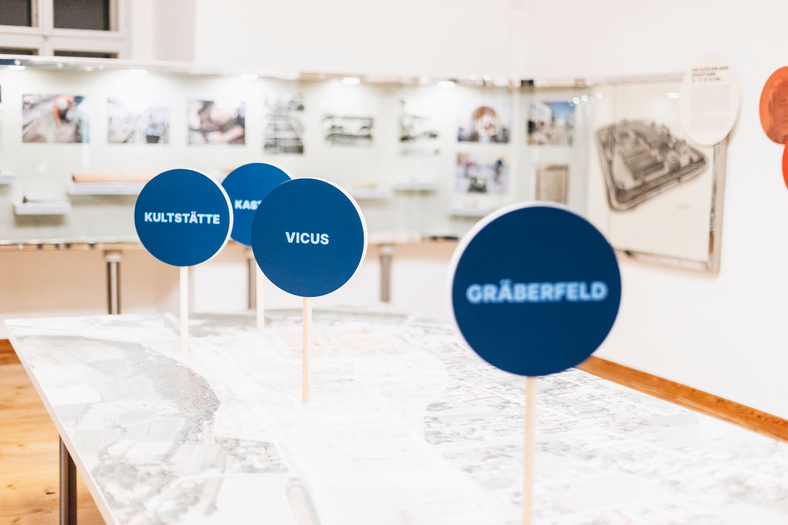 Impression aus der Ausstellung „Traismaurer Schätze“ Modell des römischen Traismauers mit blauen Stationsschildern „Kultstätte“, „Vicus“ und „Gräberfeld“