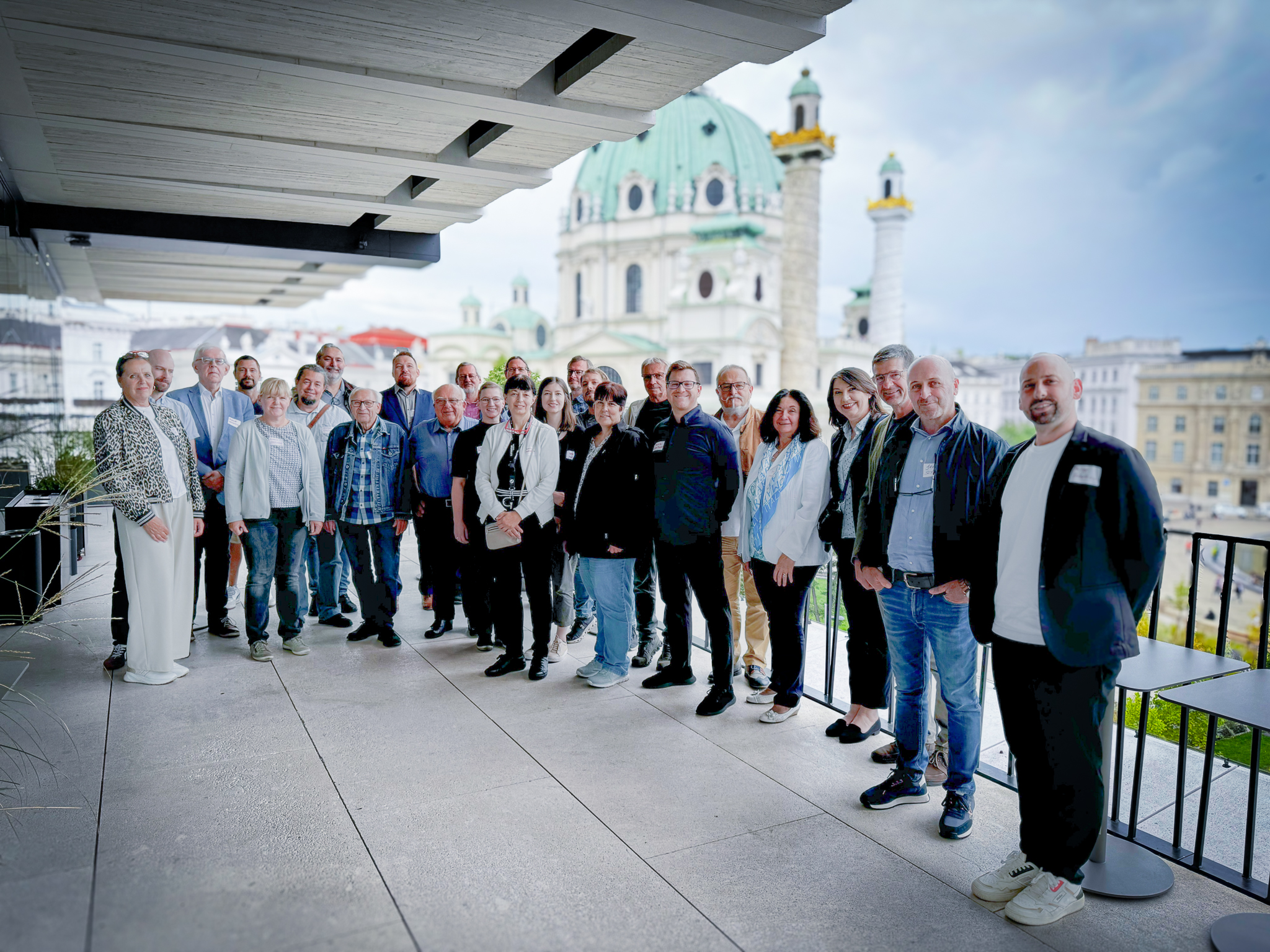 Gruppenfoto der Teilnehmerinnen und Teilnehmer des Netzwerktreffens 2025 des Vereins Donaulimes auf einer Terrasse mit Blick auf die Karlskirche in Wien