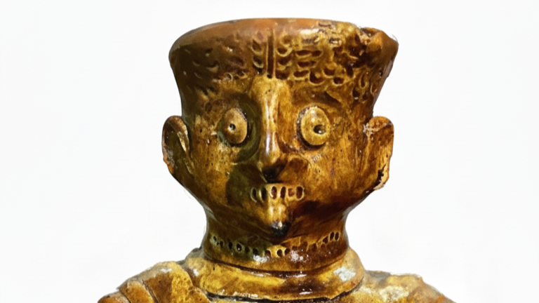 Braun glasierter anthropomorpher Keramikkrug aus Mautern an der Donau: Nahaufnahme des menschlich gestalteten Kopfes mit großen runden Augen, sorgfältig modellierten Haaren und Bart, geritzten Verzierungen und einem Mundloch.